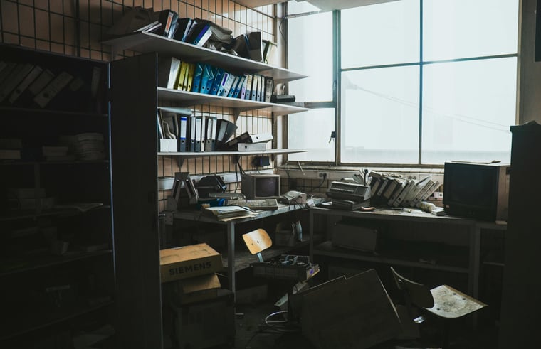 Messy office desk with multiple rows of binders on shelves 